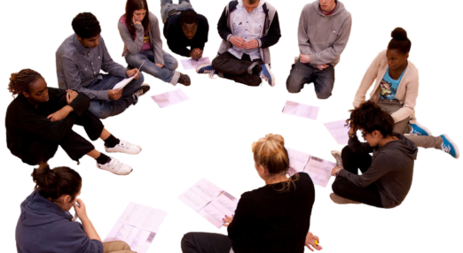 11 young people sat in a circle reading a play with scripts