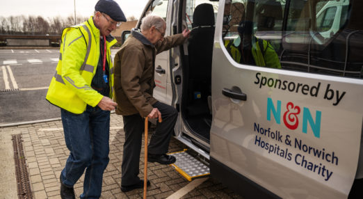 Man with walking stick being helped into a minibus by a volunteer