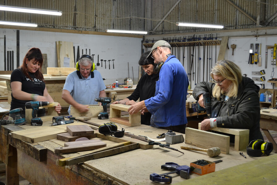 5 adults in workshop doing woodwork projects